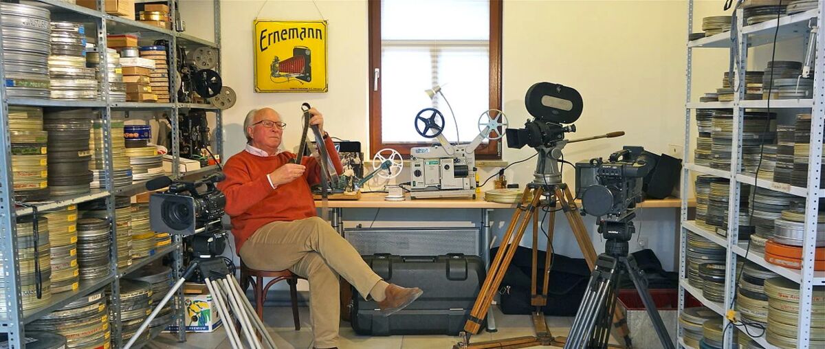 Bild eines älteren Mannes, der in einem Raum mit Regalen voller alter Filmrollen sitzt